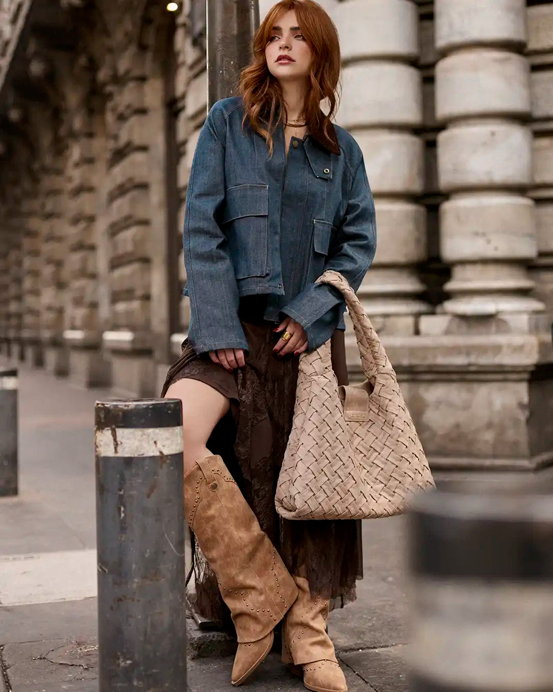 Mujer luce un outfit urbano con chaqueta de mezclilla oversize, botas altas beige y bolso trenzado cafe de Steve Madden, estilo boho en tendencia.