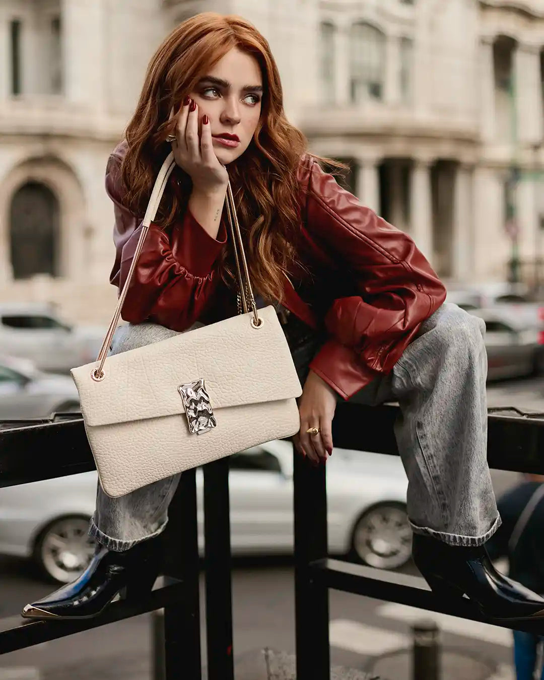 Mujer con chaqueta de cuero roja y bolso blanco y botas vaqueras negras Steve Madden, look urbano moderno.
